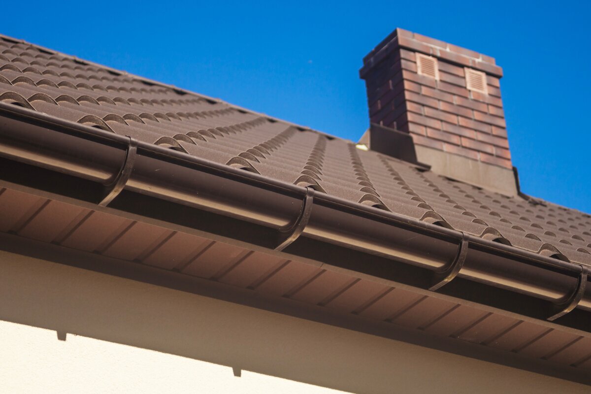 Half-round brown gutter on tile roof with chimney